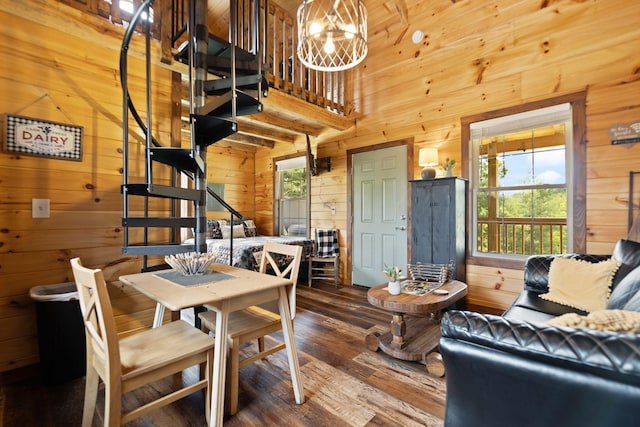 dining area with wooden walls, wood finished floors, stairs, a towering ceiling, and a notable chandelier