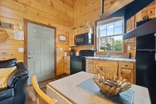 kitchen featuring a sink, wooden walls, black appliances, and light countertops