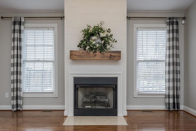 room details with wood finished floors, a fireplace with flush hearth, visible vents, and baseboards