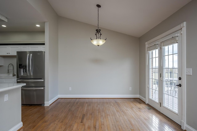 unfurnished dining area featuring vaulted ceiling, wood-type flooring, a sink, and baseboards