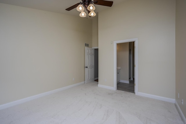 unfurnished room with visible vents, a towering ceiling, light carpet, ceiling fan, and baseboards