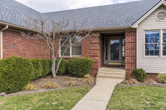 view of exterior entry with brick siding and roof with shingles