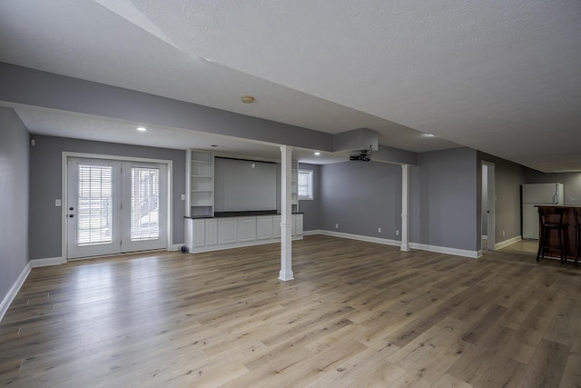 unfurnished living room with light wood-style floors, plenty of natural light, baseboards, and a textured ceiling