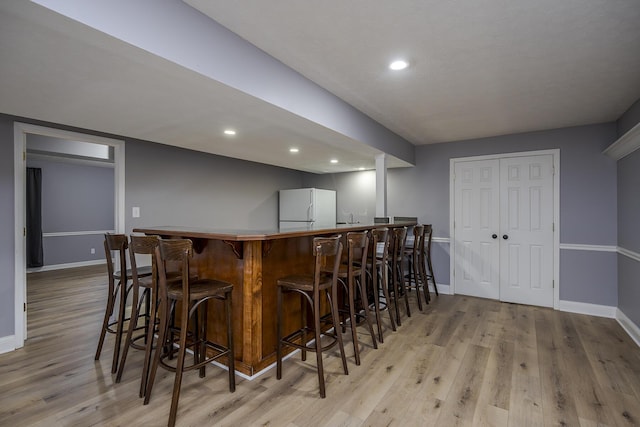 bar with freestanding refrigerator, indoor wet bar, light wood-style flooring, and baseboards