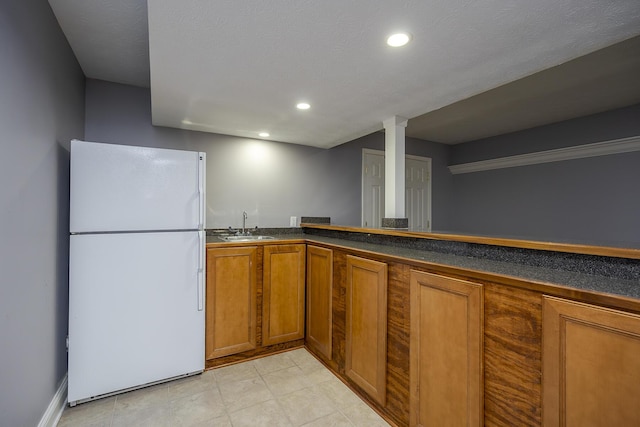 kitchen featuring dark countertops, recessed lighting, brown cabinetry, freestanding refrigerator, and a sink