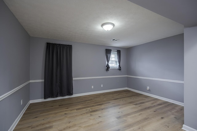 unfurnished room with baseboards, a textured ceiling, visible vents, and wood finished floors