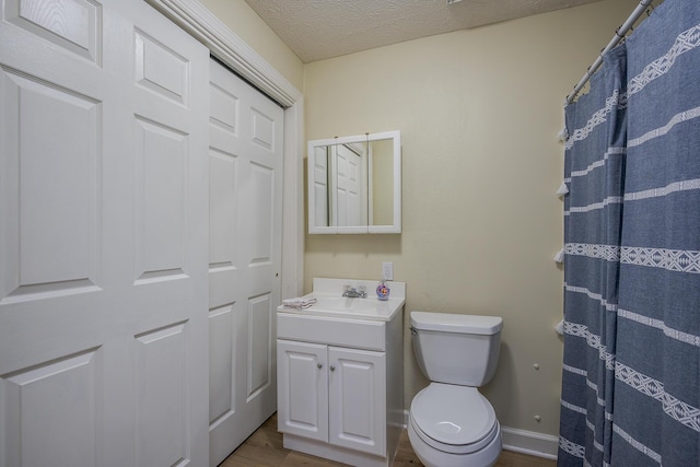 bathroom featuring baseboards, toilet, wood finished floors, a textured ceiling, and vanity