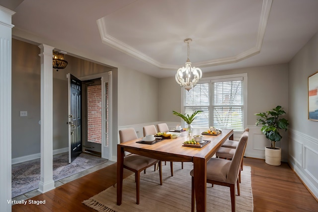 dining room with a raised ceiling, a wainscoted wall, wood finished floors, a decorative wall, and a notable chandelier