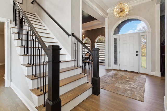 foyer with a chandelier, wood finished floors, a towering ceiling, baseboards, and ornamental molding