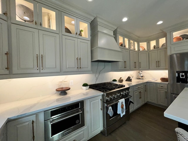 kitchen with stainless steel appliances, premium range hood, dark wood-type flooring, and backsplash