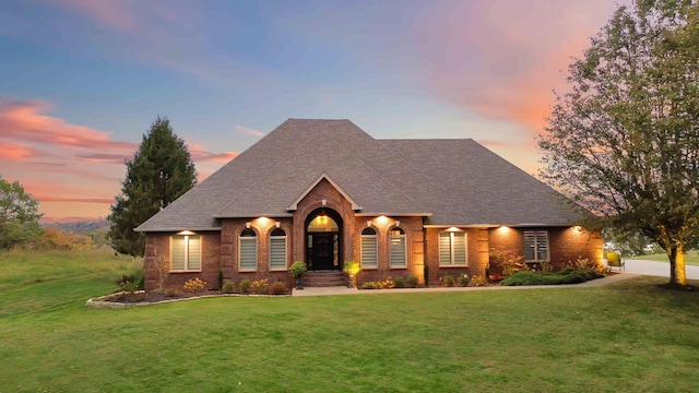 view of front of property with a front lawn, a shingled roof, and brick siding