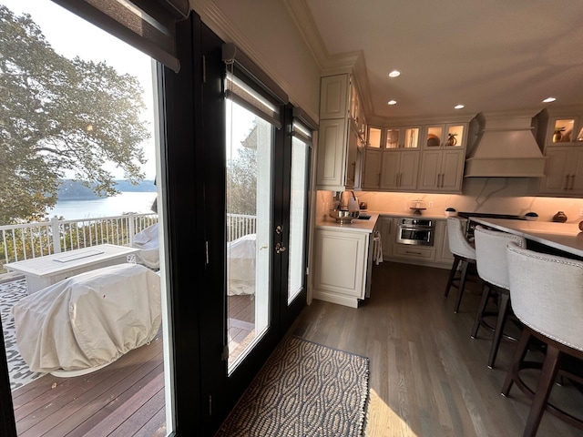 kitchen featuring dark wood-style floors, tasteful backsplash, light countertops, custom range hood, and glass insert cabinets