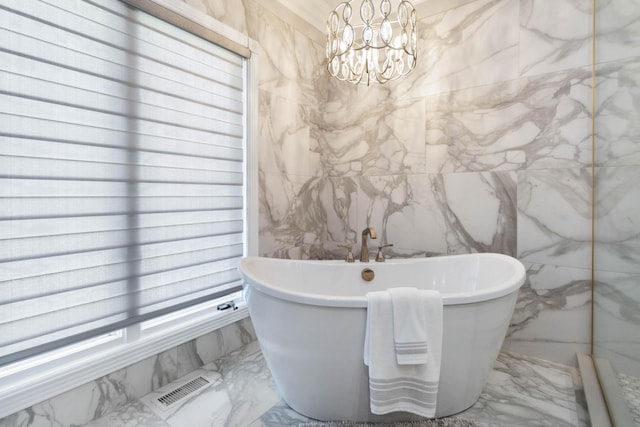 bathroom with stone wall, a freestanding tub, visible vents, marble finish floor, and an inviting chandelier