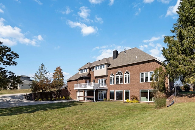 back of house featuring brick siding, a yard, a chimney, and a balcony