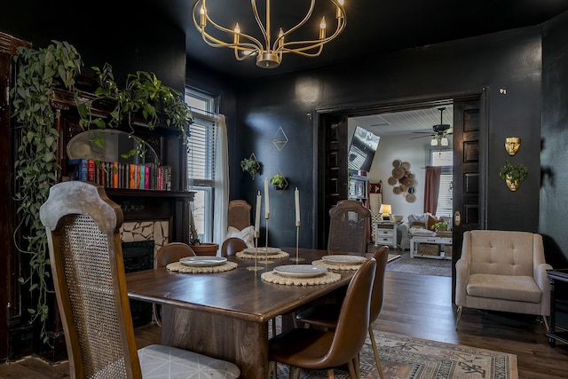 dining area featuring ceiling fan with notable chandelier, a fireplace, and wood finished floors