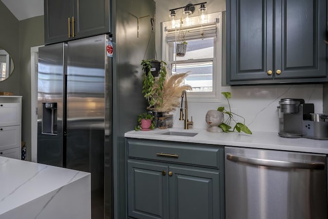 kitchen with light stone counters, stainless steel appliances, a sink, gray cabinets, and tasteful backsplash