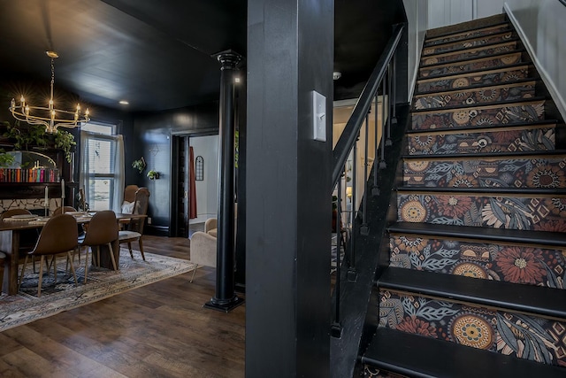 staircase with an inviting chandelier, wood finished floors, and ornate columns