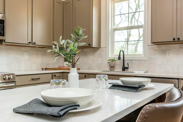 kitchen featuring tasteful backsplash, stainless steel appliances, a sink, and light stone counters