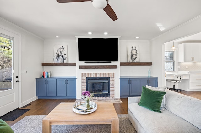 living area with dark wood finished floors, recessed lighting, ornamental molding, a ceiling fan, and a brick fireplace