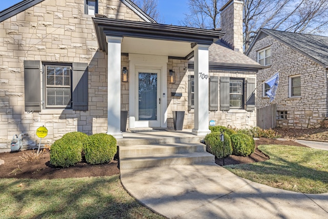 view of exterior entry featuring stone siding, a chimney, and roof with shingles