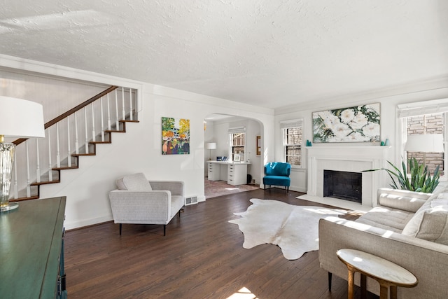 living area with arched walkways, visible vents, stairway, a fireplace with flush hearth, and wood finished floors