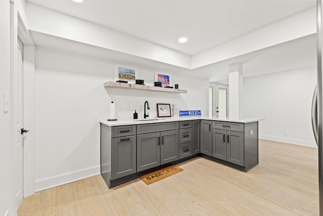 kitchen with gray cabinetry, a peninsula, a sink, baseboards, and light wood finished floors