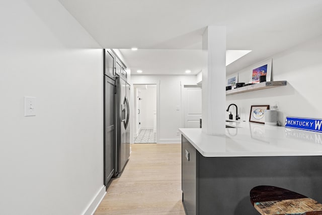 kitchen with a peninsula, baseboards, light wood-style floors, light countertops, and stainless steel refrigerator with ice dispenser