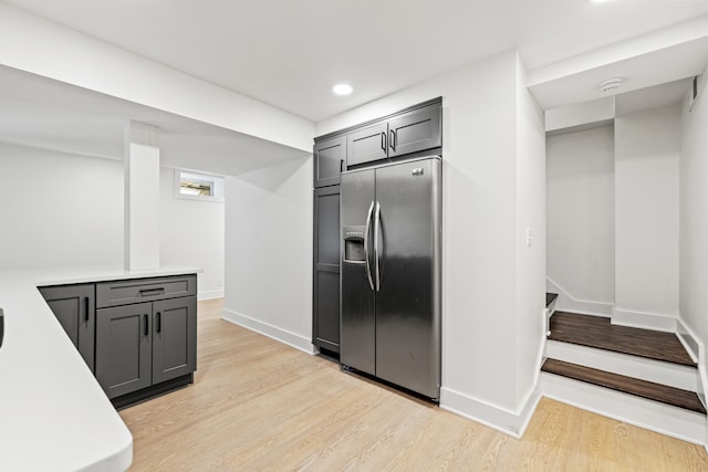 kitchen with light countertops, light wood-type flooring, stainless steel fridge, and baseboards