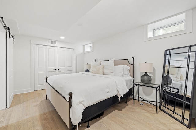 bedroom with a barn door, visible vents, light wood-type flooring, multiple windows, and a closet