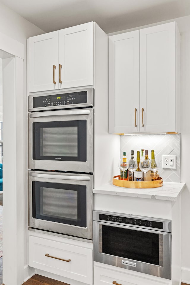 kitchen featuring light stone counters, white cabinetry, decorative backsplash, and stainless steel double oven