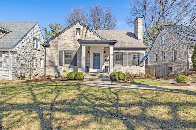 view of front of home with stone siding, roof with shingles, a chimney, and a front lawn