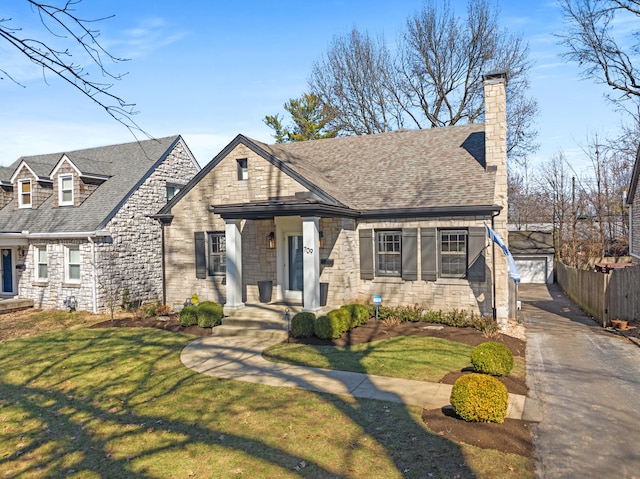 view of front of home with stone siding, a shingled roof, a front yard, and an outdoor structure