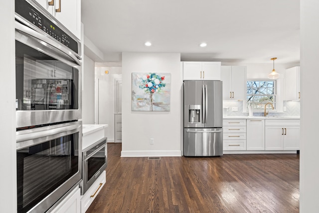 kitchen featuring dark wood-style flooring, stainless steel appliances, light countertops, backsplash, and white cabinetry