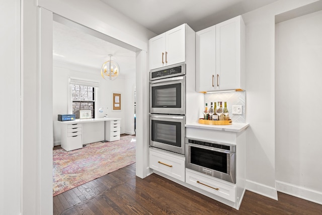 kitchen featuring stainless steel double oven, dark wood-style flooring, white cabinetry, light countertops, and tasteful backsplash