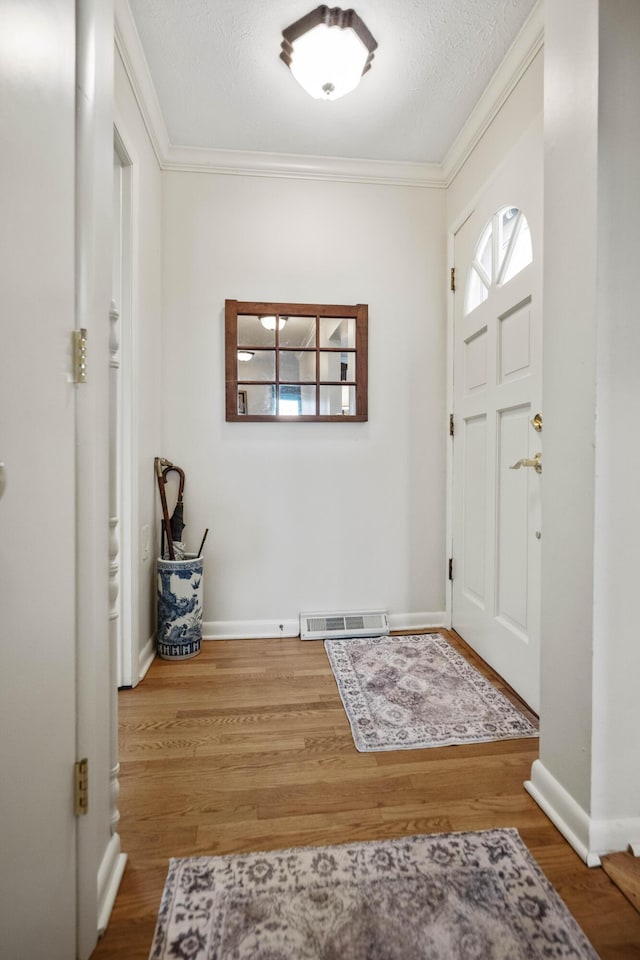 entrance foyer featuring baseboards, wood finished floors, visible vents, and crown molding