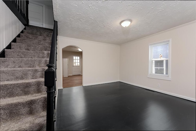 unfurnished room featuring arched walkways, a textured ceiling, baseboards, and stairs