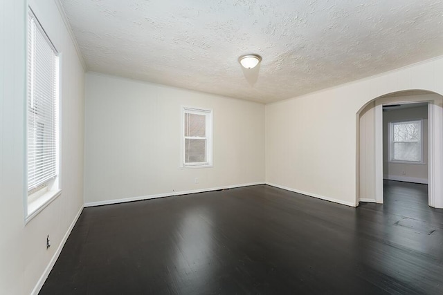 empty room with arched walkways, a textured ceiling, baseboards, and wood finished floors