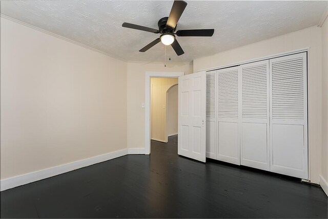 unfurnished bedroom featuring arched walkways, dark wood-style flooring, a closet, a textured ceiling, and baseboards