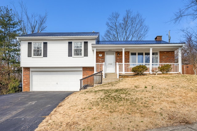 split level home featuring covered porch, a chimney, metal roof, and brick siding