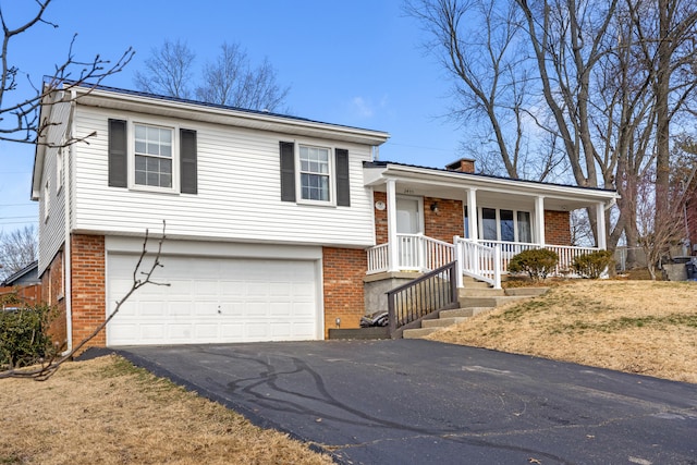 split level home featuring brick siding, a chimney, a porch, a garage, and driveway