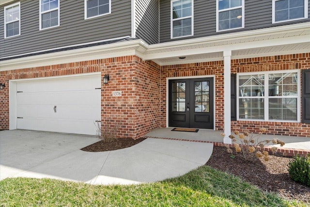 entrance to property with french doors, brick siding, an attached garage, and concrete driveway