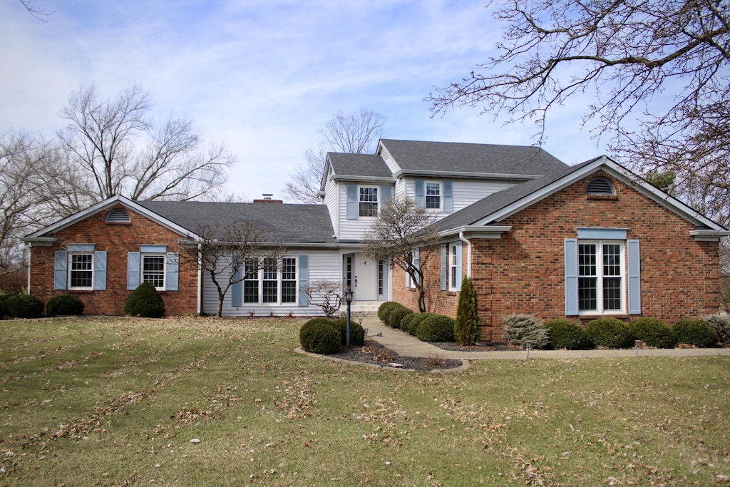 traditional home featuring brick siding, roof with shingles, and a front lawn