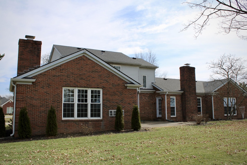 back of property with a patio area, a lawn, brick siding, and a chimney