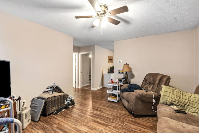 living room featuring baseboards, a textured ceiling, a ceiling fan, and wood finished floors