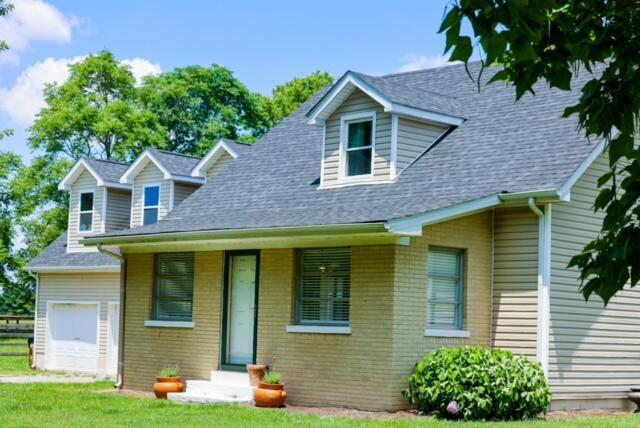 new england style home featuring a shingled roof, brick siding, and a front lawn