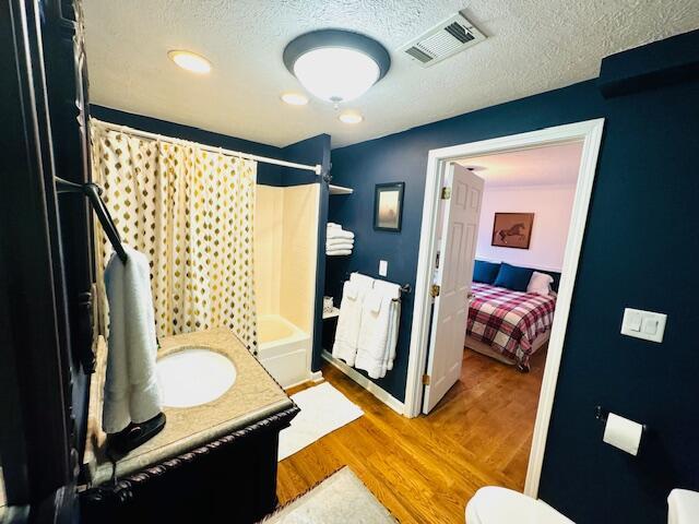 bathroom featuring shower / bath combination with curtain, visible vents, a textured ceiling, and wood finished floors