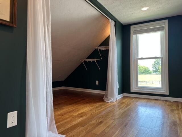 bonus room featuring light wood-type flooring, vaulted ceiling, a textured ceiling, and baseboards