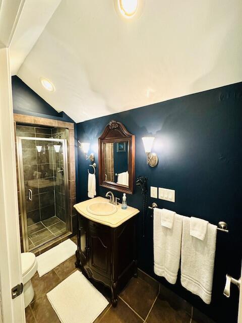 full bath featuring tile patterned flooring, toilet, vanity, vaulted ceiling, and a stall shower