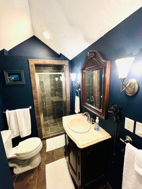 bathroom with toilet, tile patterned floors, vaulted ceiling, vanity, and a shower stall