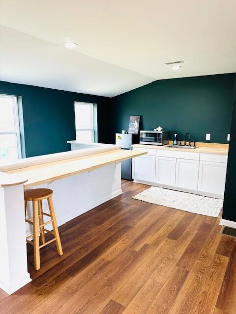 kitchen with lofted ceiling, wood finished floors, a sink, white cabinetry, and stainless steel microwave